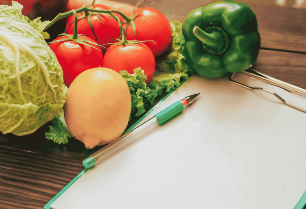 a variety of fruits and vegetables next to a pen and paper representing meal planning