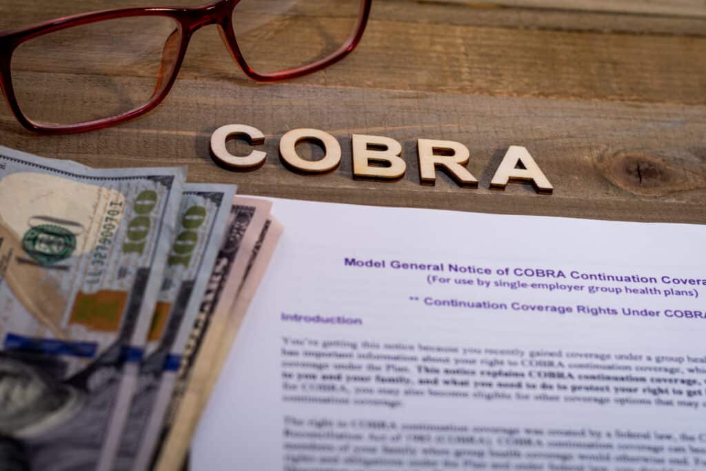 glasses, cobra, money, and a paper with a notice of cobra insurance representing what is cobra insurance