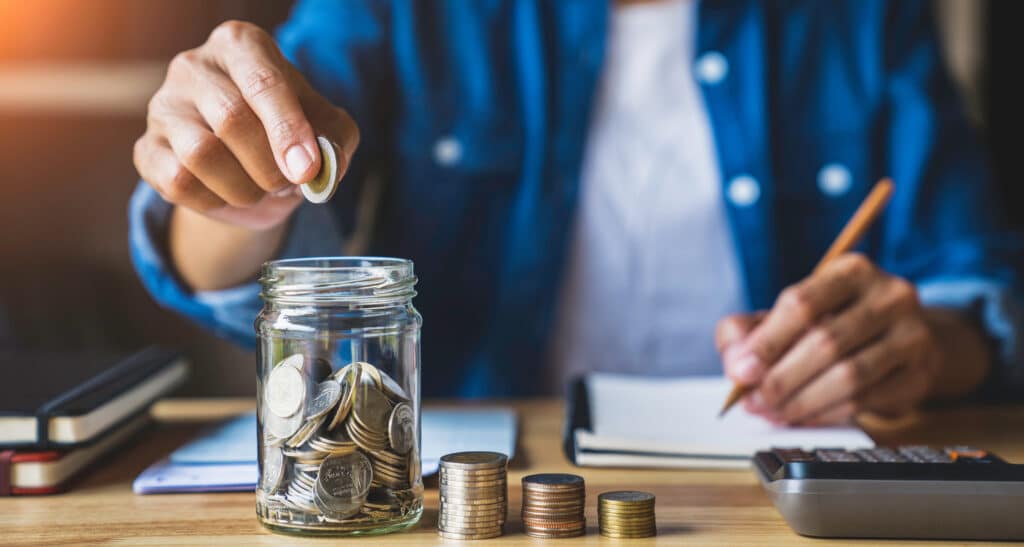 woman puts a coin in a jar to save money for the future. after retirement and record keeping of income, expenditure, savings and financial concepts.