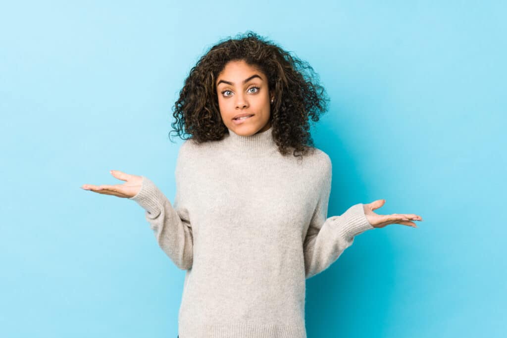 A confused lady standing against a blank blue background, appearing as though she has many questions from market analysts about stocks.