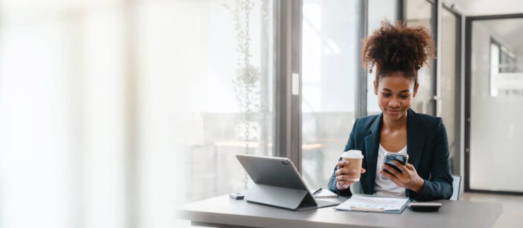 A woman holding her coffee and phone, reading about the stock exchange, winning, and the booming trading market.
