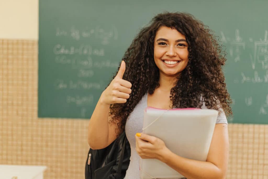 A cheerful woman holding a folder with one hand and giving a thumbs-up with the other hand.