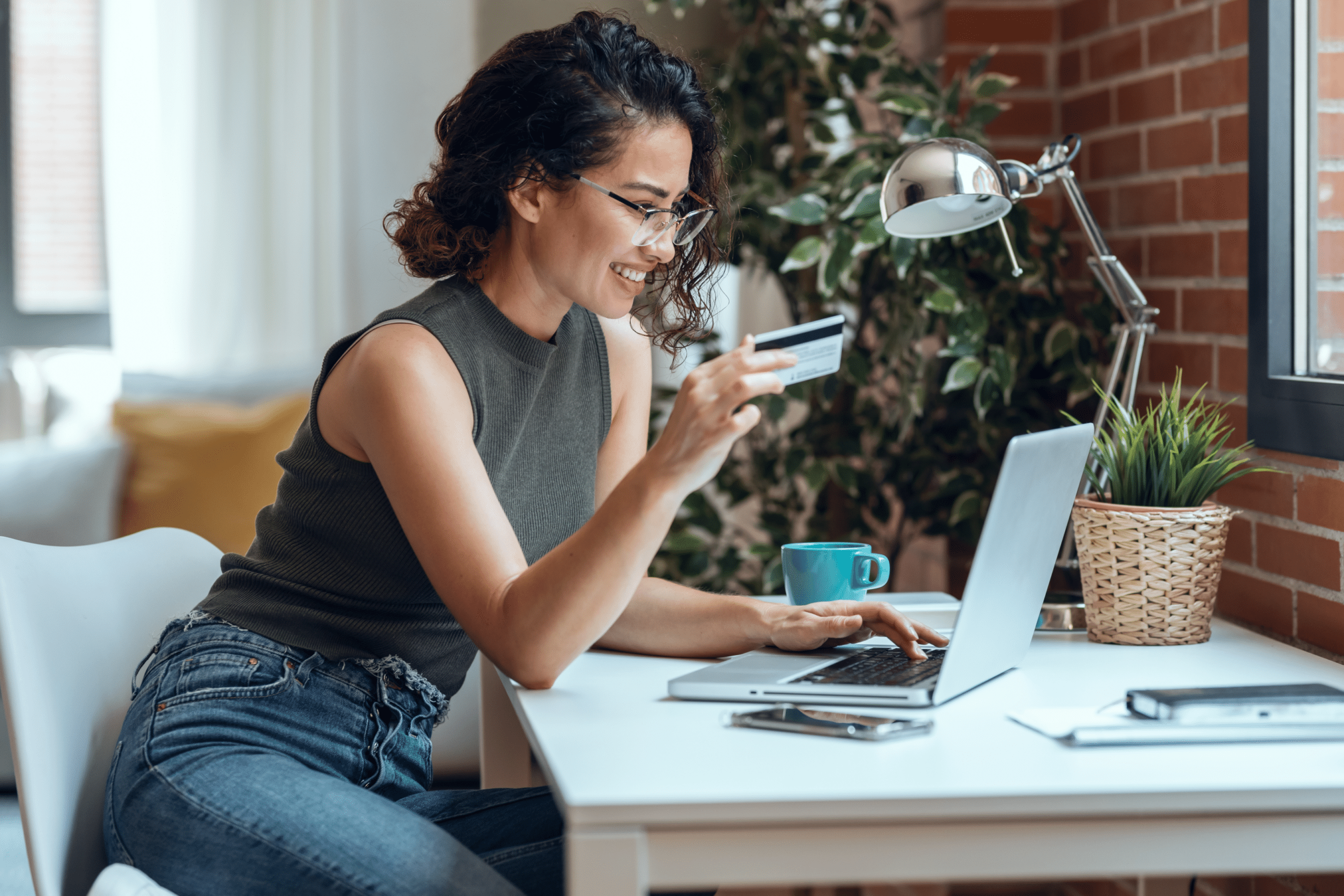 Woman holding white credit card for shopping online with computer while sitting in living room at home.