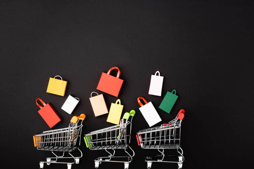 Top view of toy carts with colorful shopping bags on black background representing what can I sell to make money