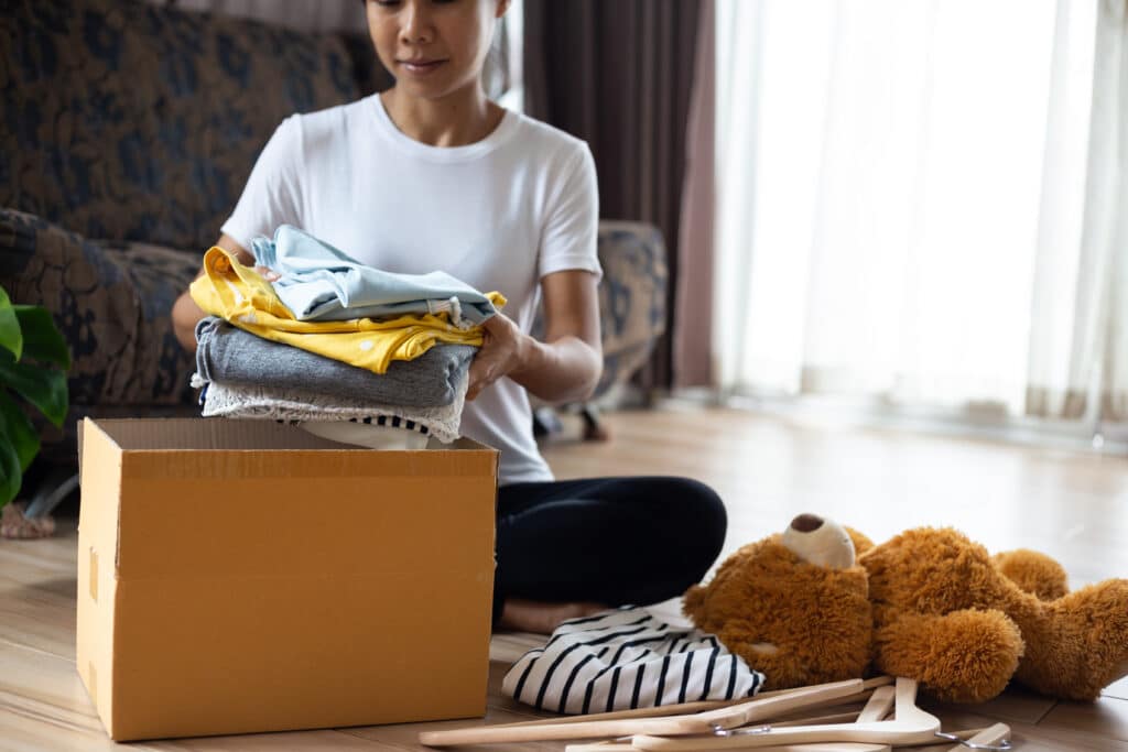 Woman holding Clothes with Donate Box In her room, Donation Concept.