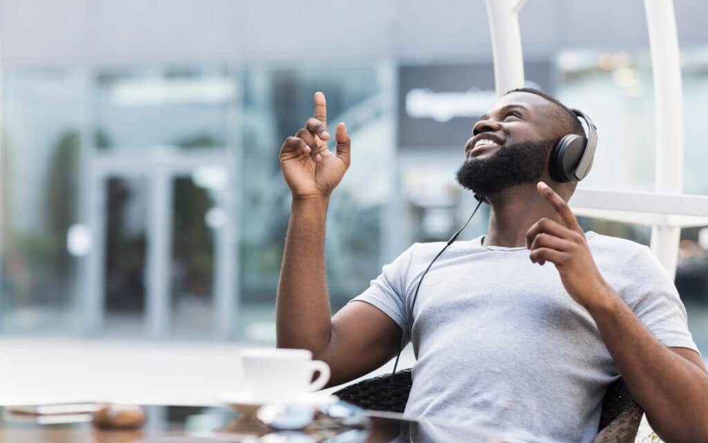 Young african american guy enjoying music in headphones and smiling in cafe, panorama, free space